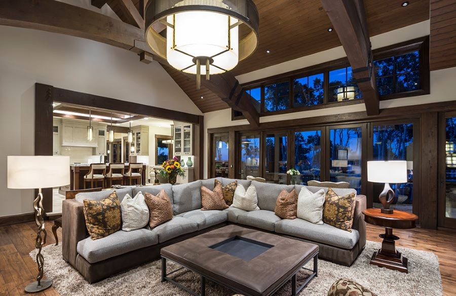 A home with an open floor plan, numerous light fixtures, and windows overlooking trees at dusk.